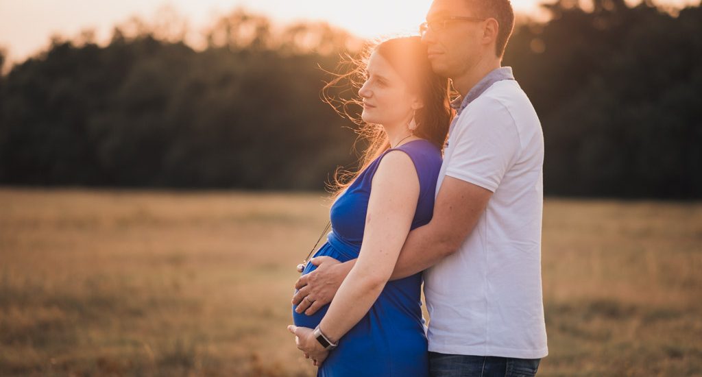 Couple enlacé avec les mains sur le ventre de la femme enceinte qui porte une robe bleue