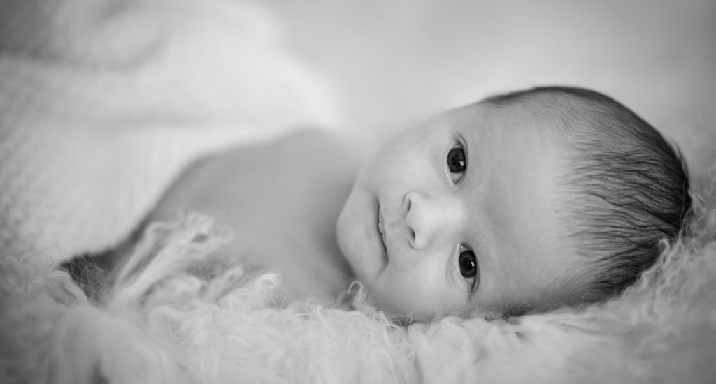 Photo en noir et blanc, style baby posing du bébé Victor. Bébé est dans un couffin blanc en laine alpaga.. La photo est épurée.