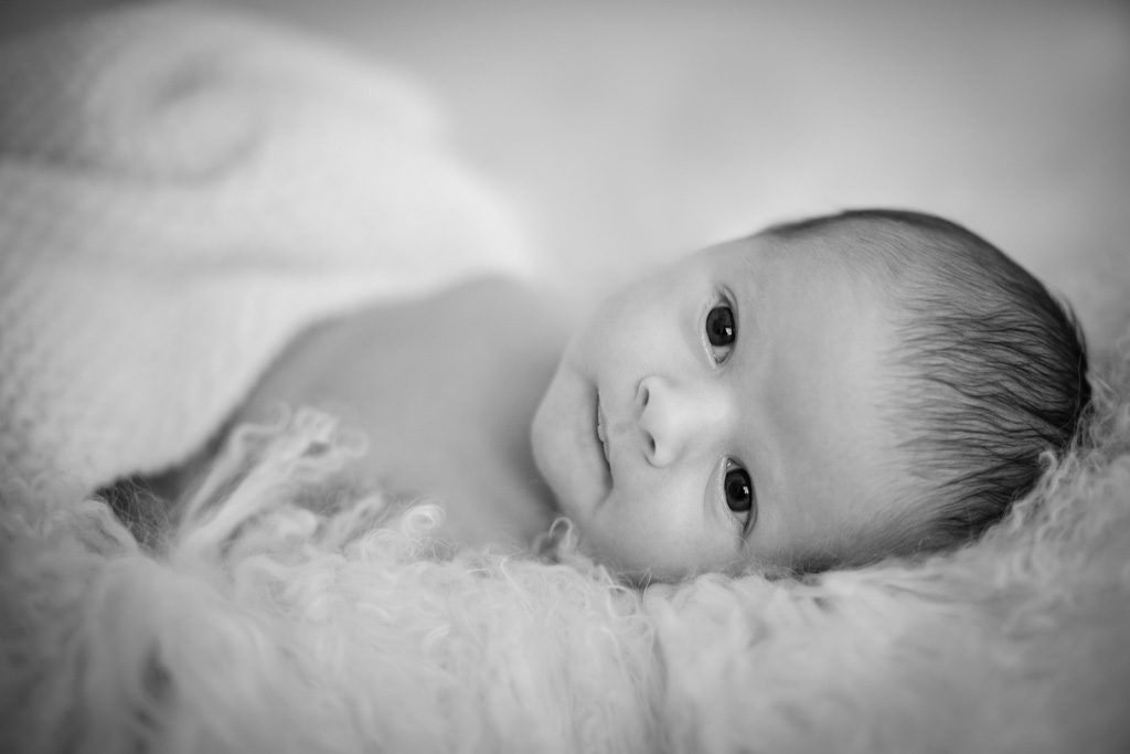 Photo en noir et blanc, style baby posing du bébé Victor. Bébé est dans un couffin blanc en laine alpaga.. La photo est épurée.