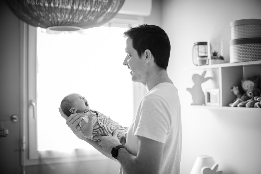 Photo du bébé en train de bailler porté par son papa. La photo est en noir et blanc.