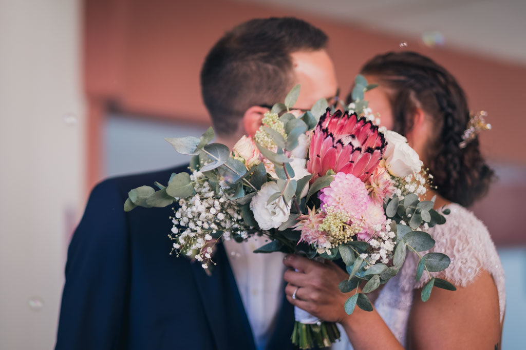 Couple de mariés qui s'embrassent cachés derrière le bouquet de la mariée