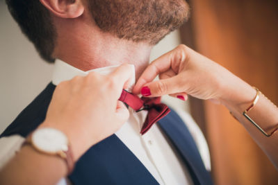 Gros plan sur le nœud papillon bordeaux du futur marié en plein préparatifs