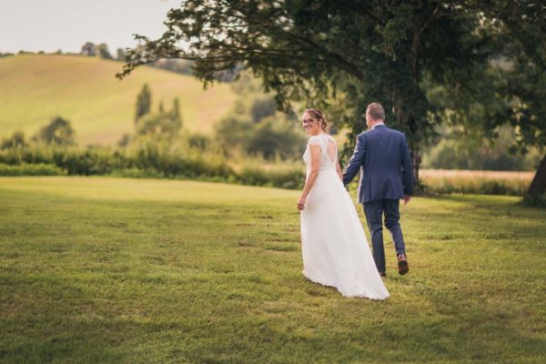 Couple de mariés qui marchent dans la campagne, la mariée se retourne et nous regarde