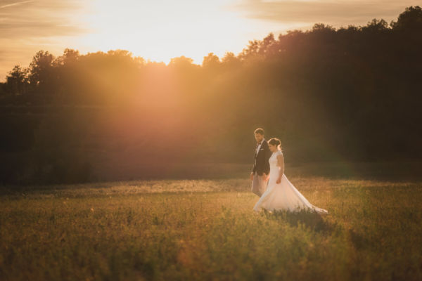 Couple de mariés qui marchent dans un champ au coucher du soleil