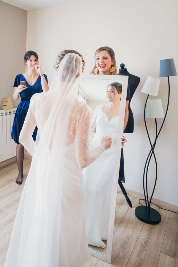 La mariée se regarde en robe dans un miroir avec ses deux témoins qui l'observent