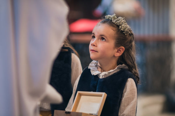 A l'église, une petite fille avec une couronne de fleurs tient dans ses main un coffret en bois contenant les alliances des futurs mariés