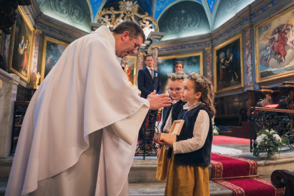 A l'église le prêtre bénit les alliances qui sont dans un coffret en bois tenue par une petite fille