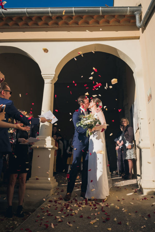 Les mariés s'embrassent à la sortie de l'église sous des jets de pétales de roses