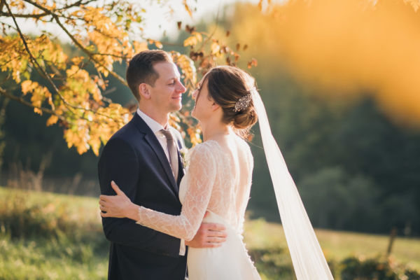 Les mariés sont face à face sous des arbres avec des feuilles jaunes d'automne